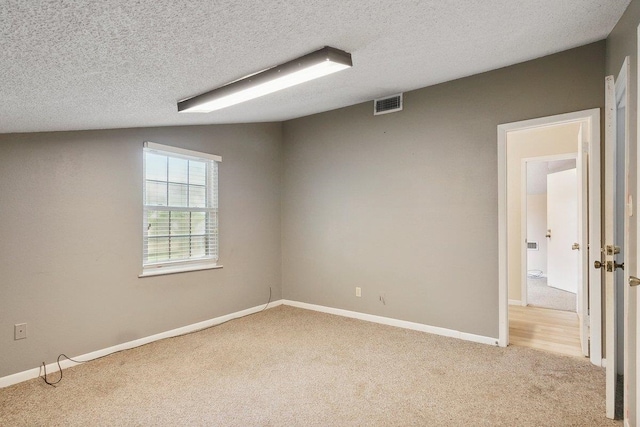 empty room featuring a textured ceiling, light colored carpet, and vaulted ceiling