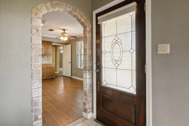 entrance foyer featuring a textured ceiling, ceiling fan, and ornamental molding