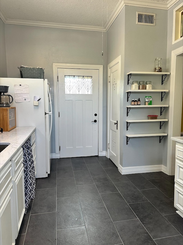 interior space featuring white refrigerator, crown molding, dark tile patterned floors, and a textured ceiling