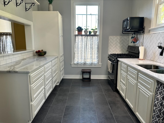 kitchen featuring backsplash, light stone counters, sink, dark tile patterned flooring, and black gas range