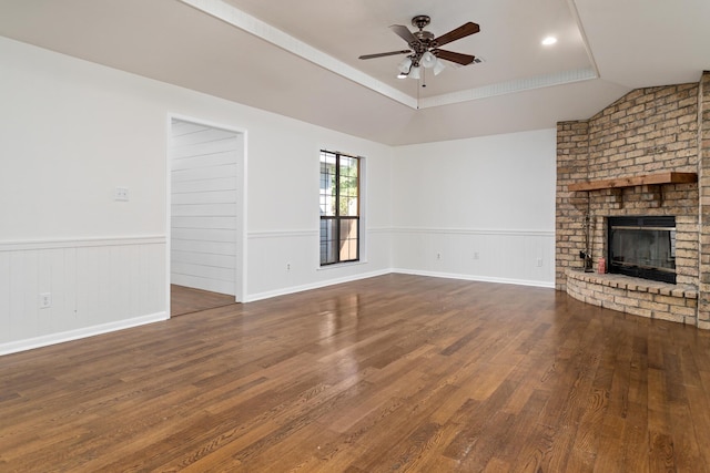 unfurnished living room featuring dark wood-type flooring, vaulted ceiling, a brick fireplace, ceiling fan, and a tray ceiling