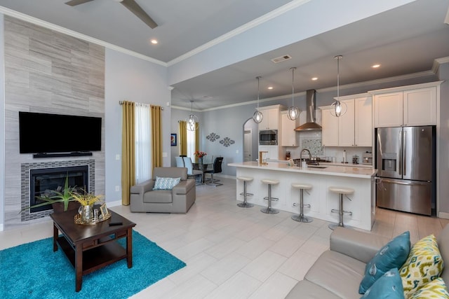 living room featuring a tile fireplace, a ceiling fan, visible vents, baseboards, and ornamental molding