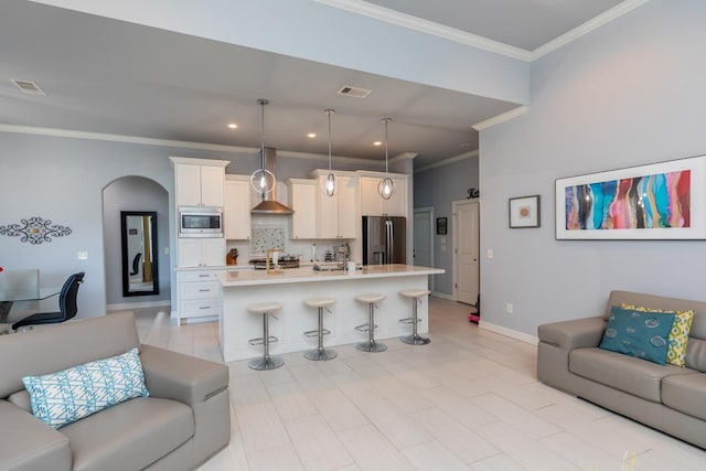 kitchen featuring arched walkways, a breakfast bar area, open floor plan, appliances with stainless steel finishes, and wall chimney exhaust hood