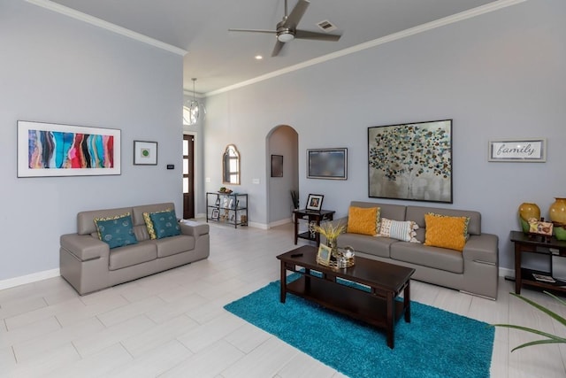 living area with arched walkways, baseboards, ceiling fan, ornamental molding, and a high ceiling