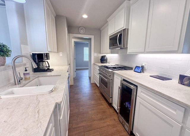 kitchen with beverage cooler, stainless steel appliances, a sink, and white cabinetry