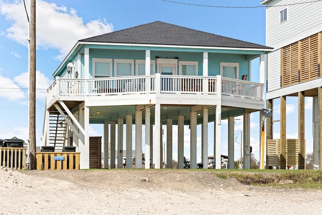 coastal inspired home with a carport, covered porch, roof with shingles, and stairs