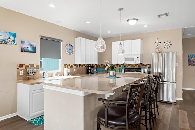 kitchen with white microwave, a kitchen island, visible vents, freestanding refrigerator, and decorative backsplash