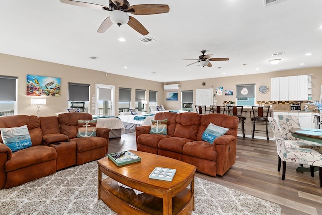 living area with an AC wall unit, light wood-style flooring, visible vents, and recessed lighting