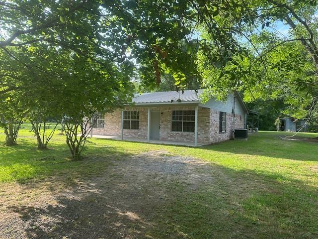 back of house featuring a lawn, central AC unit, stone siding, and metal roof