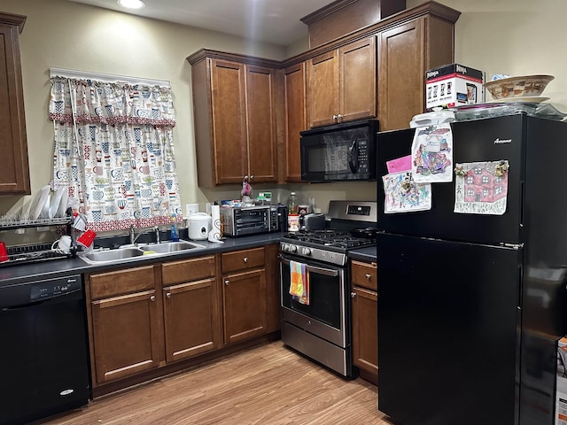 kitchen with dark countertops, a sink, a toaster, black appliances, and light wood-style floors