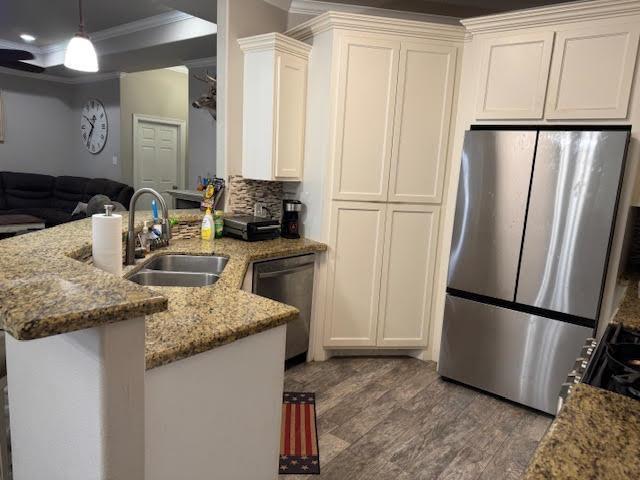 kitchen with open floor plan, a peninsula, light stone countertops, stainless steel appliances, and a sink