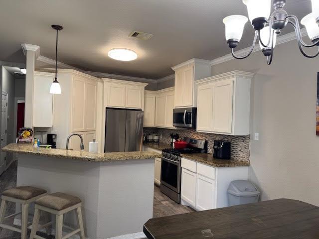 kitchen featuring visible vents, a kitchen breakfast bar, stainless steel appliances, white cabinetry, and backsplash