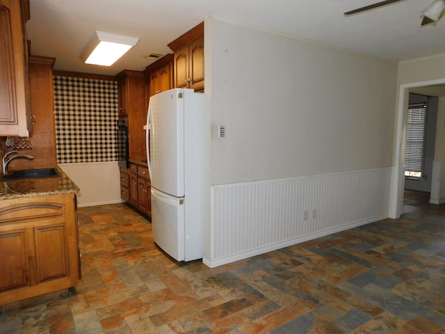 kitchen with white refrigerator, sink, ceiling fan, dark stone countertops, and ornamental molding