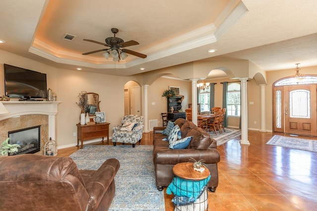 tiled living room featuring a tray ceiling, ceiling fan, decorative columns, and ornamental molding