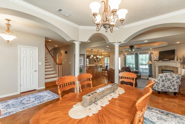 tiled dining space featuring a textured ceiling, decorative columns, ceiling fan with notable chandelier, and ornamental molding