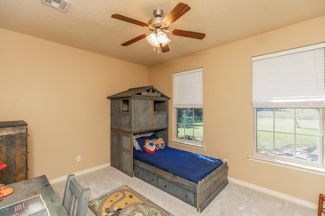 bedroom with ceiling fan, light carpet, and a textured ceiling