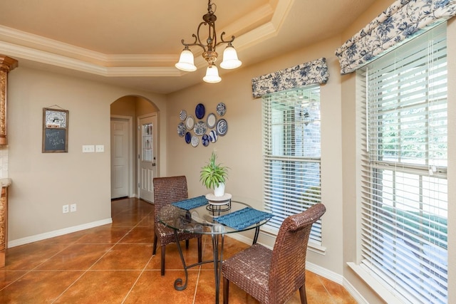 tiled dining space with a raised ceiling, ornamental molding, and an inviting chandelier