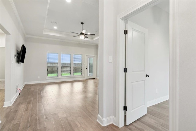 hall with a tray ceiling, light hardwood / wood-style floors, and ornamental molding