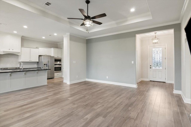 kitchen with stainless steel appliances, tasteful backsplash, a tray ceiling, white cabinets, and light wood-type flooring