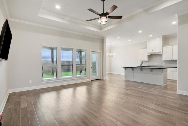 unfurnished living room with a raised ceiling, crown molding, light hardwood / wood-style floors, and ceiling fan with notable chandelier