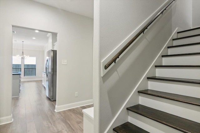 stairs with hardwood / wood-style floors, crown molding, and a chandelier