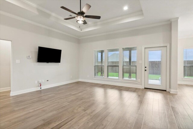 unfurnished living room with a tray ceiling, ceiling fan, light hardwood / wood-style floors, and ornamental molding