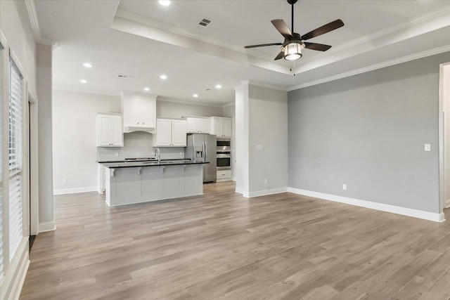 kitchen with backsplash, a kitchen island with sink, light hardwood / wood-style flooring, white cabinetry, and stainless steel appliances