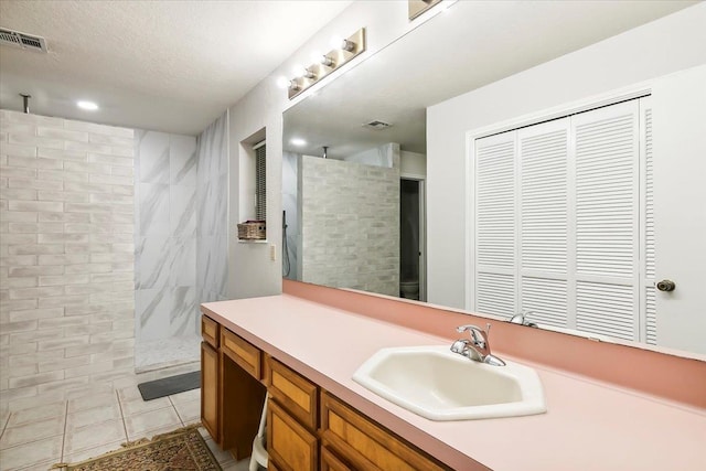 bathroom with tile patterned flooring, vanity, tiled shower, and a textured ceiling