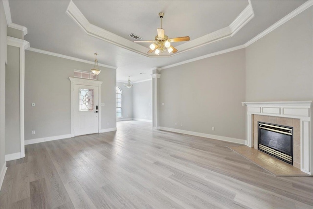 unfurnished living room with a tray ceiling, a tiled fireplace, ceiling fan with notable chandelier, visible vents, and light wood-style floors