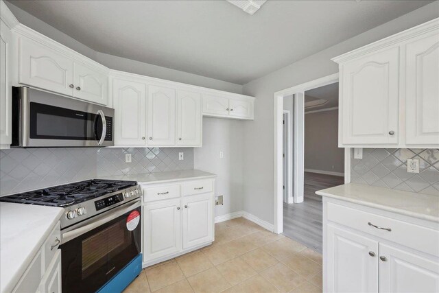 kitchen with light tile patterned flooring, light countertops, stainless steel appliances, baseboards, and white cabinets