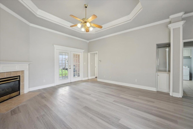 unfurnished living room featuring a raised ceiling, washer / clothes dryer, light wood-style floors, ceiling fan, and a tile fireplace