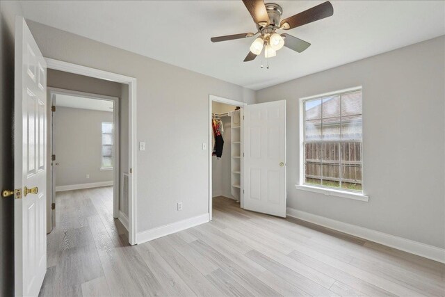 unfurnished bedroom with baseboards, light wood-style flooring, and a spacious closet