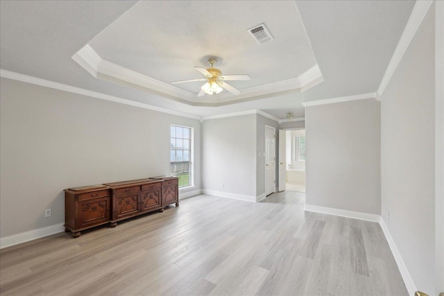 empty room featuring light wood-type flooring, a raised ceiling, ceiling fan, and visible vents