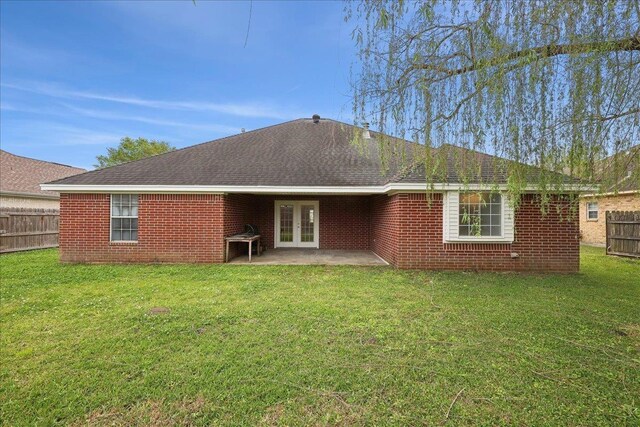 rear view of property featuring french doors, fence, brick siding, a patio, and a lawn