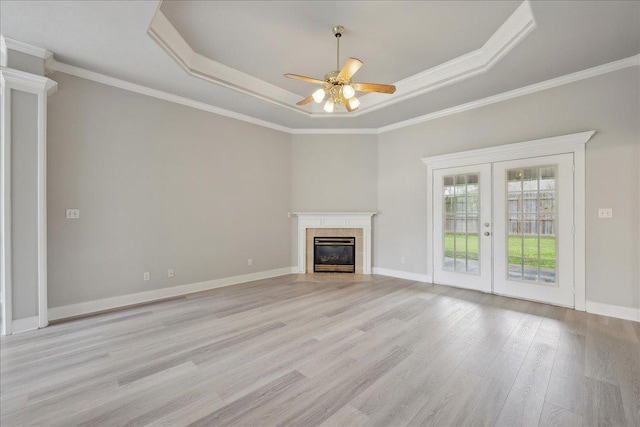 unfurnished living room featuring crown molding, a tray ceiling, french doors, light wood-style floors, and ceiling fan