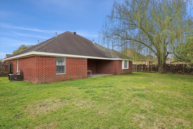 rear view of property featuring central AC, brick siding, a fenced backyard, and a yard