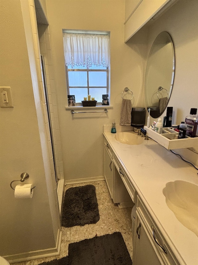 bathroom with double vanity, a shower with shower door, baseboards, and a sink