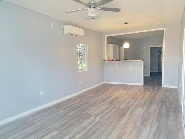 unfurnished living room with light wood finished floors, a ceiling fan, baseboards, and an AC wall unit