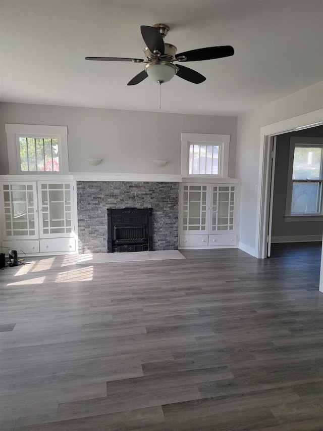 unfurnished living room with dark hardwood / wood-style floors, ceiling fan, a fireplace, and a wealth of natural light