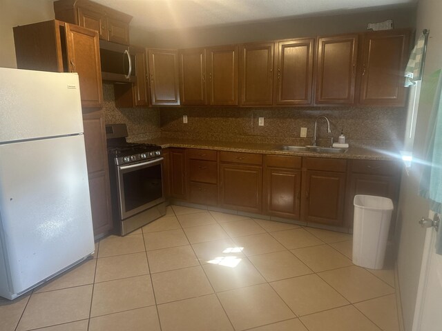 5041 9th St, Port Arthur, TX 77642 - kitchen featuring stainless steel appliances, a sink, tasteful backsplash, light tile patterned floors, and brown cabinets