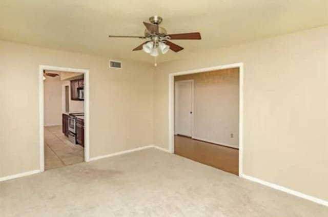 unfurnished room with light carpet, a ceiling fan, visible vents, and baseboards