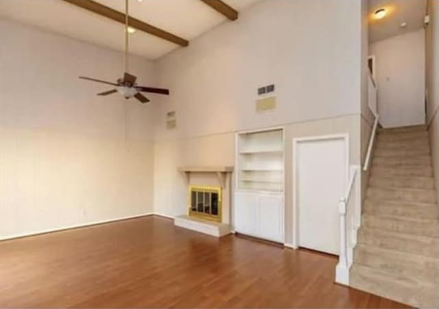 unfurnished living room with beam ceiling, a glass covered fireplace, a ceiling fan, wood finished floors, and high vaulted ceiling