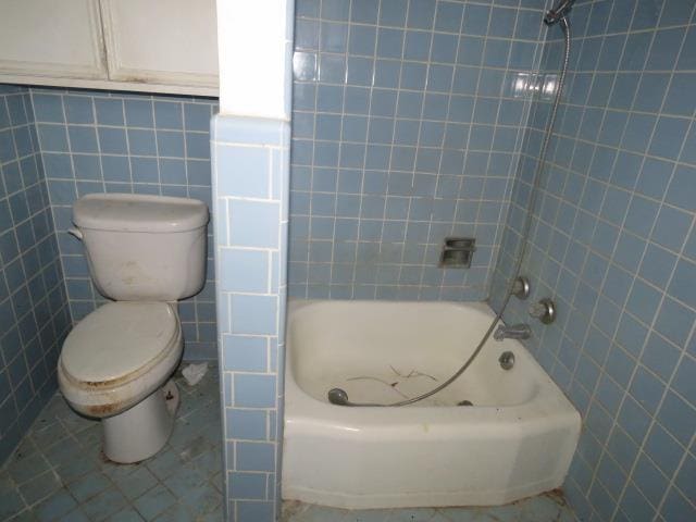 bathroom featuring tile patterned floors, tiled shower / bath combo, tile walls, and toilet