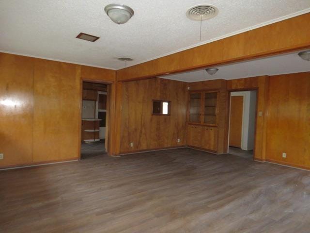 empty room with wood walls, dark hardwood / wood-style flooring, ornamental molding, and a textured ceiling