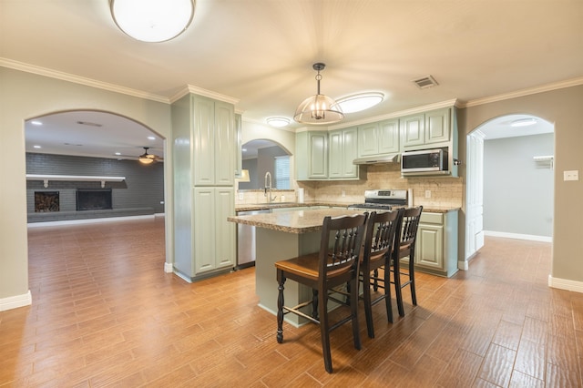 5269 Fairview Dr, Orange, TX 77630 - kitchen featuring arched walkways, appliances with stainless steel finishes, under cabinet range hood, a center island, and crown molding