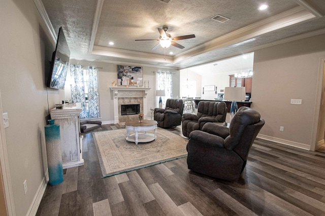 living room with dark hardwood / wood-style flooring, a raised ceiling, ceiling fan, crown molding, and a fireplace