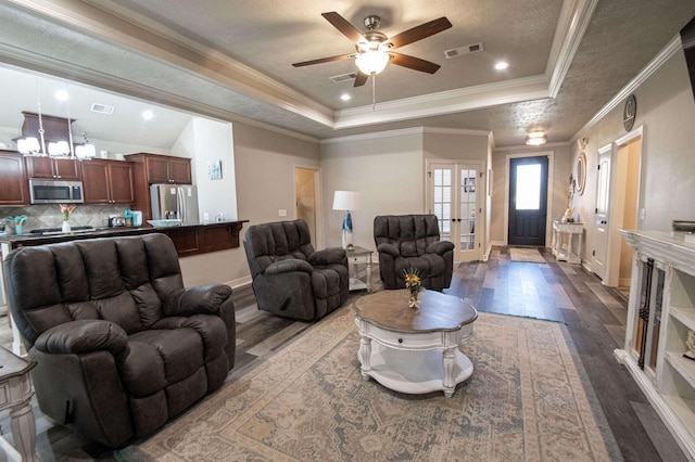 living room with a raised ceiling, crown molding, ceiling fan, and dark wood-type flooring