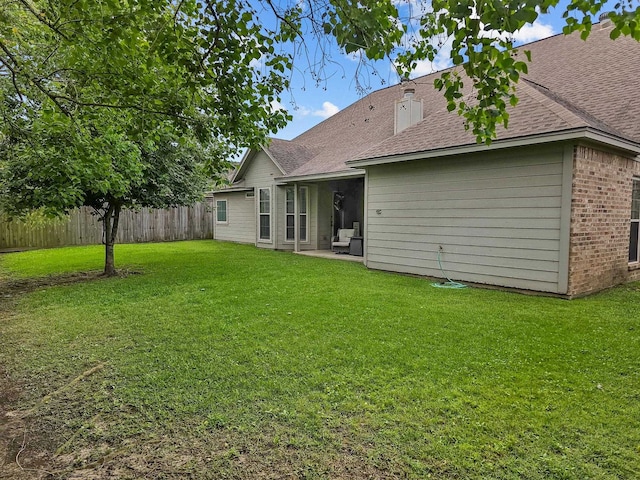 back of property with brick siding, roof with shingles, a yard, and fence
