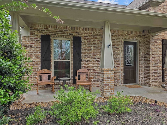 doorway to property with covered porch and brick siding