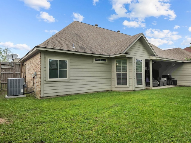 back of house with a lawn, roof with shingles, central AC unit, and brick siding